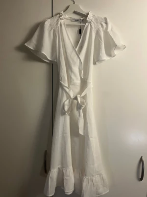 Vit omlottklänning från NA-KD - Säljer en vit omlottklänning från NA-KD med volangkant nertill, korta vida ärmar och knytband i midjan. Den är helt ny, med prislapp kvar🩷🩷