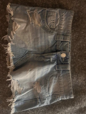 Ljus sliten kjol med fransar - Säljer en ljusblå kjol med slitningar och fransiga kanter. Kjolen har klassiska fickor fram och bak, samt bälteshällor. Perfekta för sommaren och ger en avslappnad streetstyle-look.