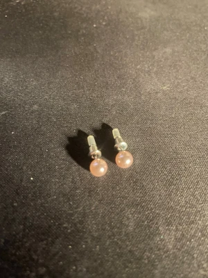 Rosa pärlörhängen i silverfärg - Säljer ett par stilrena örhängen med ljusrosa pärlor och silverfärgade detaljer. Klassisk rund form och diskret design som passar till många olika stilar. Perfekta för dig som gillar enkla men snygga accessoarer. OBS! Materialet är okänt, kan ej garantera att det är rostfritt.