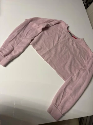 Ljusrosa croppad långärmad topp - Trendig ljusrosa croppad topp med långa ärmar och rund hals. Tillverkad i mjukt bomullsmaterial som känns skönt mot huden. Perfekt att matcha med höga jeans eller kjol för en cool och avslappnad look.