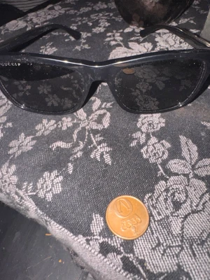 Svarta solglasögon från Gucci - Snygga svarta solglasögon från Gucci med klassisk rektangulär form. Bågarna har Guccis ikoniska röd-gröna rand på sidan och logga i guld. Tillverkade i blankt syntetmaterial som ger en lyxig känsla. ..Äktq vara inga några billiga kopior. 