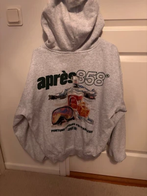 Grå hoodie med tryck - Säljer en grå hoodie från cotton on med stor färgglad print på ryggen. På framsidan finns en mindre logga och text. Hoodien har huva och ribbade muddar. Perfekt för dig som gillar unik streetwear och lite baggy kläder.