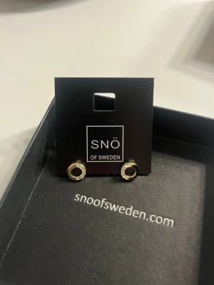 Guldörhängen Snö of Sweden Colline - Snygga små örhängen från Snö of Sweden i modellen Colline. De är runda, guldfärgade och har gnistrande klara stenar runt hela cirkeln. Perfekta för dig som gillar stilrena men ändå glittriga accessoarer.