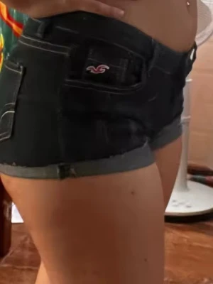Mörkblå jeansshorts från Hollister - Säljer ett par mörkblå jeansshorts från Hollister med uppvikta benslut och klassisk femficksdesign. Shortsen har låg midja och en liten broderad logga på fickan. Perfekta för varma dagar och enkel att matcha med olika toppar.