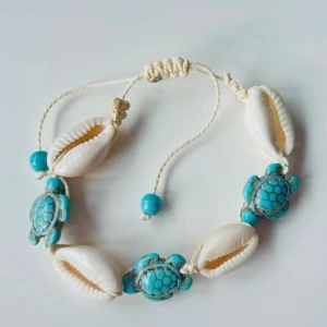 Snäckarmband med turkosa sköldpaddor - Armband med vita snäckor, turkosa pärlor och detaljerade sköldpaddor i turkost. Justerbart band i beige snöre ger en bohemisk känsla. Perfekt accessoar för strandvibbar och somrig stil.