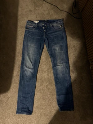 Blå slim fit jeans med slitningar - Säljer ett par blå slim fit jeans med snygga slitningar och tvättade detaljer. Klassisk femficksmodell med dragkedja och knapp i midjan. Jeansen har en modern passform och är perfekta för en avslappnad stil. Materialet är mjukt denim i bomull.