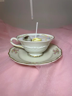 Doftljus i vaniljdoft i en tekopp med fat med blommig design  - Det här ljuset är gjort av återanvändbara material. Tekoppen är köpt secondhand och stearinet är från kyrkor som tänkte slänga det. Det här ljuset har en svag doft utav vanilj, så känsliga även kan använda det. Det här ljuset har även torkade blommor på som dekoration. 