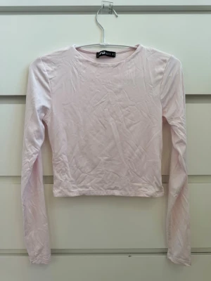 Ljusrosa långärmad croppad topp - New Yorker - Säljer en enkel och stilren ljusrosa långärmad topp från New Yorker. Modellen är croppad med rund halsringning och har en mjuk, stretchig känsla. Perfekt att matcha med höga jeans eller kjol för en clean look. (Sorry för hur skrynklig den är på bilden) 💗