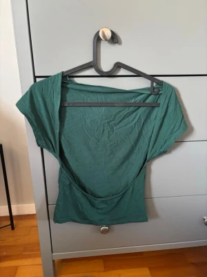 Grön topp med öppen rygg - Snygg grön t-shirt med korta ärmar och öppen rygg. Modellen är loose fit och toppen är tillverkad i mjuk bomull, perfekt för en avslappnad och trendig stil. Passar dig som gillar enkla men coola plagg.