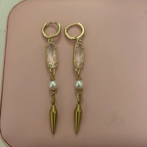 Guldörhängen med pärldetalj - Säljer dessa snygga örhängen i guldfärg med en vit pärldetalj och spetsig hängande metallpendel. Perfekta för dig som vill ha något unikt och trendigt till din stil. Örhängena har klicklås och en cool mix av material. Säljer pga ingen användning!💕