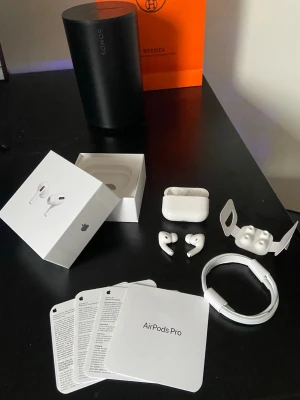 AirPods Pro - Säljer ett par vita Apple AirPods Pro med laddningsetui, extra silikonpluggar och laddningskabel. Hörlurarna har en stilren och kompakt design i plast och levereras med originalförpackning och manualer. Perfekta för dig som vill ha grymt ljud och brusreducering.