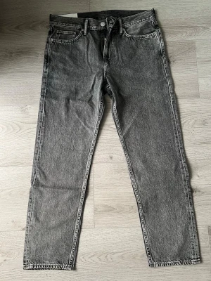 Grå relaxed fit jeans från H&M - Säljer ett par gråa relaxed fit jeans från H&M med klassisk femficksmodell och raka ben. Jeansen har en tvättad look och är tillverkade i bomull. Perfekta för en avslappnad och trendig stil.