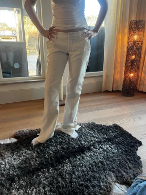 Vita raka kostymbyxor - Snygga vita kostymbyxor med rak passform och klassiska fickor fram och bak. Byxorna har bälteshällor och stängs med dragkedja och knapp. Perfekta för en clean och stilren look. Materialet ser ut att vara bomull eller en bomullsblandning.