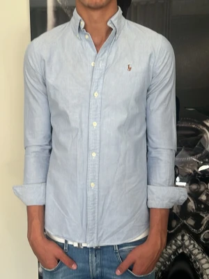 Ljusblå skjorta från Polo Ralph Lauren - Klassisk ljusblå skjorta från Polo Ralph Lauren med button-down krage och broderad logga på bröstet. Skjortan har långa ärmar, vita knappar och är tillverkad i mjuk bomull. Perfekt till jeans eller chinos för en clean och stilren look. Priset kan diskuteras vid en snabb affär!🙌🤝