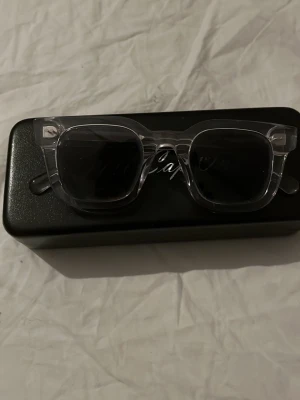 All Cap one - Använda någon enstaka gång nypris 499kr Säljer ett par trendiga solglasögon med transparent, fyrkantig båge och mörka glas. Kommer med ett svart fodral. Perfekta för dig som vill ha en clean och modern look.