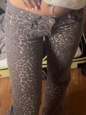 Leopardmönstrade jeans med låg midja - Säljer ett par trendiga leopardmönstrade jeans med låg midja och raka ben. Jeansen har klassisk femficksmodell och stängs med knapp och dragkedja. Perfekta för dig som vill sticka ut med ett djurmönster i garderoben.