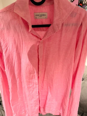 Rosa linneskjorta från John Henric - Säljer en snygg rosa skjorta från John Henric i luftigt linne. Skjortan har klassisk krage, långa ärmar och knappar framtill. Perfekt för dig som vill ha en stilren och fräsch look med en färg som sticker ut. Perfekt för sommar säljes då den har blivit förliten för mig, nypris 1000:)
