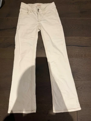 Vita bootcut jeans från Replay - Snygga vita jeans från Nelly med bootcut-modell och klassiska fem fickor. Jeansen har ljus kontrastsöm och broderade detaljer på bakfickorna. Tillverkade i ett mjukt bomullsmaterial med lite stretch för extra komfort. De är uppsydda och passar perfekt till dig som är mellan 140-155 cm lång!