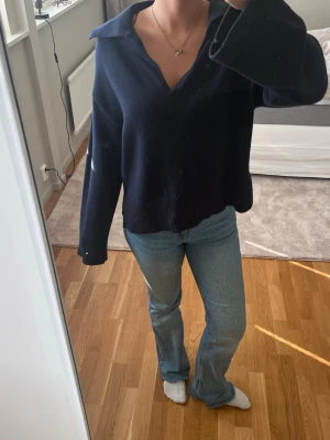 Mörkblå stickad tröja med krage - Mysig mörkblå stickad tröja med djup v-ringning och bred krage. Tröjan har långa ärmar och ribbstickad nederkant. Perfekt för lager-på-lager och passar till jeans eller kjol.