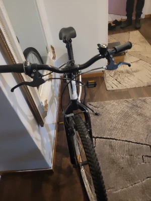 Vit mountainbike Rockrider - Säljer en vit mountainbike från Rockrider med svarta detaljer och grova däck. Cykeln har raka styren, handbromsar och stöd. Perfekt för dig som vill ha en robust cykel för både stad och terräng.