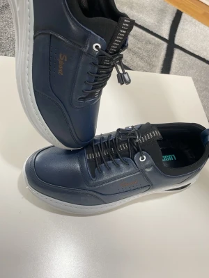 Mörkblå sneakers från Sport - Snygga mörkblå sneakers från Sport med vita sulor och svarta detaljer. Skorna har svarta snören med vita ränder och en stilren design i konstläder. Perfekta för dig som vill ha en clean och modern look till vardagsoutfiten.helt ny 