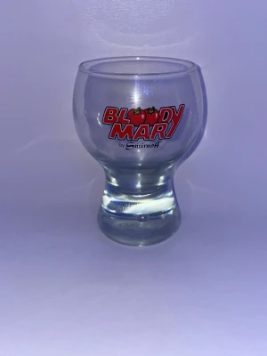 Bloody Mary glas från Smirnoff - Unikt glas med rundad form och trycket 'Bloody Mary by Smirnoff' i rött och vitt. Tillverkat i klart glas, perfekt för drinkar eller som samlarobjekt. Glaset har en stabil fot och dekorativa tomater i loggan.