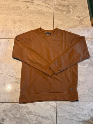 Brun sweatshirt från Blend - Säljer en brun sweatshirt från Blend med klassisk rund halsringning och ribbade muddar vid ärmslut och nederkant. Tröjan har en enkel och stilren design, perfekt att matcha med jeans eller chinos.