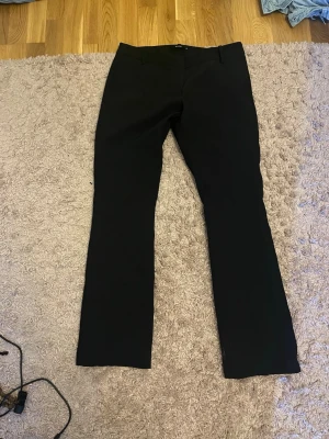 Svarta kostymbyxor från BikBok - Klassiska svarta kostymbyxor från BikBok i rak modell. Byxorna har midjehöjd och är perfekta för en clean och stilren look. Tillverkade i ett mjukt material som känns bekvämt hela dagen.