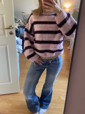 Rosa och lila randig stickad tröja  - Mysig stickad tröja från Lindex i rosa med breda lila ränder. Tröjan har en loose passform, rund halsringning och långa ärmar. Perfekt för att skapa en avslappnad och trendig look.