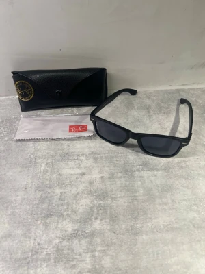 Svarta Ray-Ban solglasögon Wayfarer - Klassiska svarta Ray-Ban Wayfarer solglasögon med rektangulära bågar i plast. Kommer med originalfodral och putsduk. Snygg och tidlös modell som passar till allt och ger en cool vibe. Glasögonen är typ aldrig använda så duken och annat ligger fortfarande inplastat och original förpackningen följer med. 