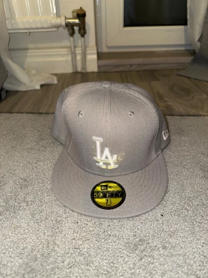 Grå LA New Era 59Fifty keps - Snygg grå keps från New Era med LA-logga broderad framtill. Modellen är 59Fifty med platt skärm och klassisk passform. Perfekt för dig som gillar streetstyle och sportiga accessoarer. Storlek : 59,6cm