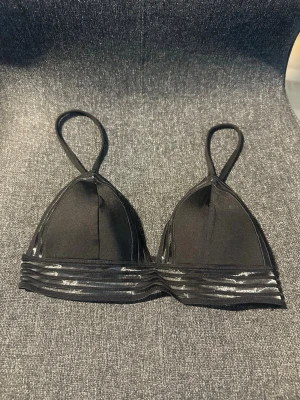 Svart bralette med transparenta detaljer - Stilren svart bralette med tunna axelband och unika transparenta ränder nedtill. Mjuk och följsam modell utan bygel, perfekt för dig som gillar enkel men snygg design. Materialet känns lent mot huden och ger en modern look.