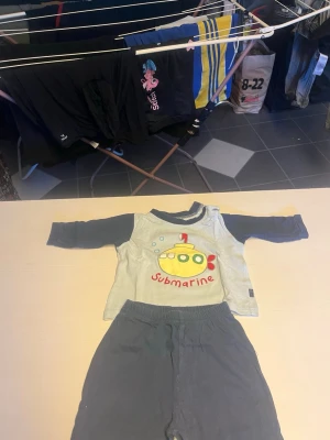 Set med ubåtstryck, långärmad & byxa - Sött set med långärmad tröja och byxa för barn. Tröjan är ljusgrå med mörkblå ärmar och har ett färgglatt ubåtstryck samt texten 'submarine' framtill. Byxorna är mörkblå med matchande ubåtstryck på benet. Mjukt och bekvämt material, perfekt för lek. Det var väldigt gulligt pyjamas.