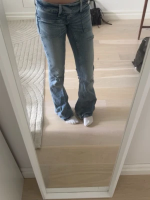 Blå lowrise bootcut jeans - Säljer ett par blå bootcut jeans från Gina Tricot med slitningar och två fickor framtill ifrån Young 14+. Knappt använda.