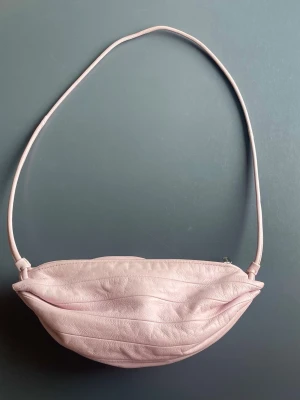 Marimekko ljusrosa Karla väska - Säljer en fin ljusrosa väska från Marimekko, en stilren och tidlös accessoar som passar perfekt till både vardag och finare tillfällen. Den mjuka rosa färgen gör väskan enkel att matcha och ger en elegant touch till outfiten.  Väskan är använd och har tecken på slitage på ytan. En del av slitaget syns på några av bilderna. Trots detta är väskan fortfarande väldigt fin och fullt användbar.  Originalpriset ligger runt 2400kr 💗 