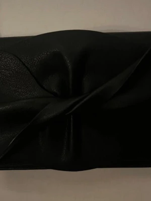Svart handväska - Stilren svart kuvertväska i konstläder med mjuk struktur och vikbar framsida. Väskan har en enkel axelrem och minimalistisk design utan synliga loggor eller detaljer. Perfekt för dig som gillar en clean och modern look.