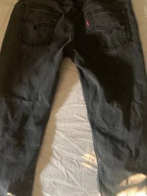 Svarta jeans från Levi's xs/s w28 L32 - Pris kan diskuteras. Säljer ett par svarta jeans från Levi's med klassisk femficksdesign och raka ben. Jeansen har tydliga bakfickor med den ikoniska Levi's-sömmen och röd etikett. Materialet är kraftig denim i bomull. Slim fit