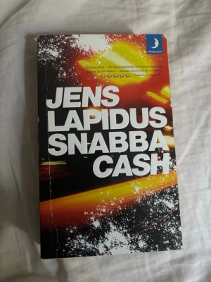 Snabba Cash av Jens Lapidus - Snabba Cash av Jens Lapidus är en spännande pocketbok med svart, vit, gul och röd omslagsdesign. Boken handlar om Stockholms undre värld och är en modern svensk thriller. Perfekt för dig som gillar kriminalromaner och actionfyllda berättelser.