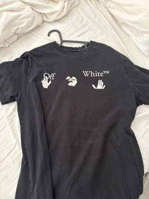 Svart Off-White t-shirt med tryck - Säljer en svart t-shirt från Off-White med ikoniskt tryck fram och stort grafiskt tryck bak med vita och gula detaljer. T-shirten har korta ärmar och normal passform. Perfekt för dig som gillar streetwear och vill sticka ut. passar xl 