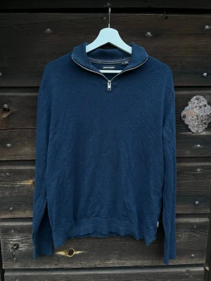 Mörkblå halvzip-tröja från Jack & Jones - Mörkblå långärmad tröja från Jack & Jones med halv dragkedja vid kragen. Tröjan har en avslappnad passform och ribbade muddar vid ärmslut och nederkant. Perfekt för lager-på-lager och enkel att matcha med jeans eller chinos.