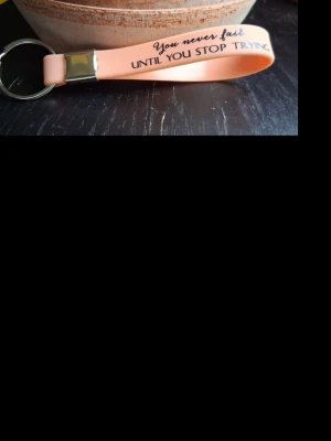 Peachfärgad nyckelring med citat - Snygg peachfärgad nyckelring i silikon med texten 'You never fail until you stop trying' tryckt i svart och blått. Metallfäste och rund nyckelring i silverfärg. Perfekt accessoar till väskan eller nycklarna.