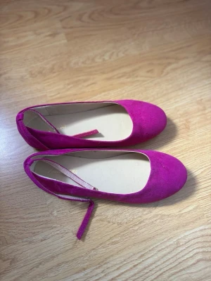 Lila ballerinaskor - Ballerinaskor med rund tå och smala snören som kan knytas runt vristen. Skorna har en mjuk ovandel i mockaimitation och platt sula. Perfekta för dig som vill sticka ut med färg och stil.