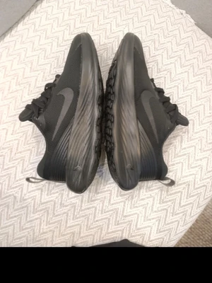 Svarta Nike sneakers Stl 44 - Säljer ett par helsvarta Nike sneakers med låg profil och diskret swoosh på sidan. Ovandelen är i meshmaterial för bra andningsförmåga och sulan är vågigt mönstrad för extra grepp. Skorna har klassisk snörning och dragflik bak.