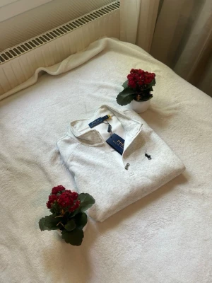 Ljusgrå quarter zip från Polo Ralph Lauren - Snygg ljusgrå tröja med quarter zip från Polo Ralph Lauren. Tröjan har en klassisk krage och den ikoniska broderade loggan på bröstet. Perfekt för en stilren och avslappnad look.