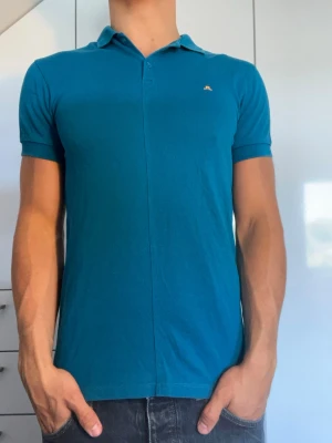 Blå pikétröja från J.Lindeberg - Blå pikétröja från J.Lindeberg. Strl S. Inga defekter. Modellen är 178 cm och väger 77 kg. Hör gärna av dig vid frågor!