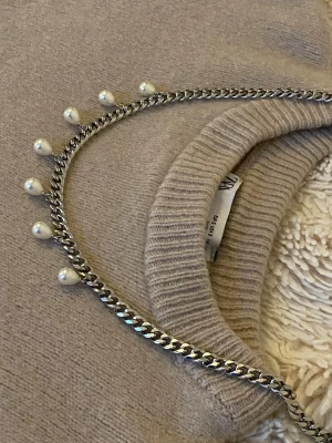 Silverfärgat halsband med pärlor - Stilrent halsband i silverfärgad rostfritt med hängande vita pärlor längs kedjan. Kedjan har en klassisk, lite chunky design som ger ett modernt intryck. Perfekt accessoar för att lyfta din outfit.