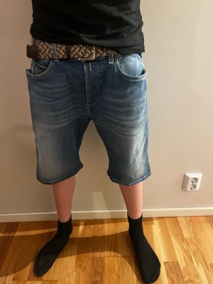 Blå jeansshorts från Replay - Säljer ett par blå jeansshorts från Replay med klassisk femficksdesign och snygga slitningar. Shortsen har normal passform och midwaist, perfekta för en avslappnad stil. Tillverkade i bomull för en skön känsla.