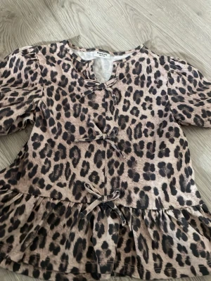 Leopardmönstrad blus från Kappahl - Säljer en leopardmönstrad blus från Kappahl med volang nedtill och dekorativa rosetter framtill. Blusen har rund halsringning och puffiga långärmar. Materialet är mjukt och lätt, perfekt för att skapa en cool look.typ helt ny💕💕använd en enstaka gång