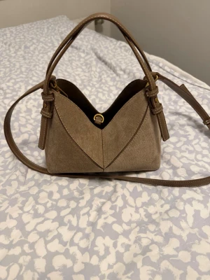 Beige handväska med axelrem från Zara - Snygg beige handväska i mockaliknande material med både handtag och justerbar axelrem. Invändigt finns ett fack med dragkedja för småsaker. 