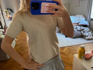 Beige kashmirtröja från Soft Goat - Kortärmad beige tröja i mjuk kashmir från Soft Goat. Tröjan har rund halsringning och ribbade kanter. Perfekt för en stilren och avslappnad look.